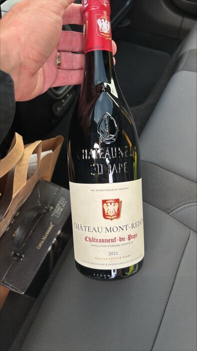 Flaska med rött vin från Château Mont-Redon, Châteauneuf-du-Pape 2021, hålls i handen i en bil.