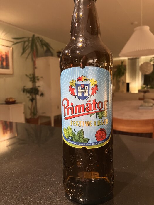 Flaska med öl av märket Primator Festive Lager på ett bord i ett vardagsrum.