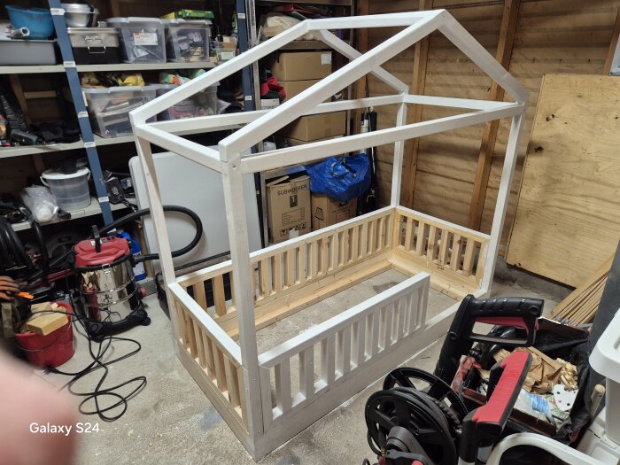 Självbyggd barnsäng i trä med husram, under konstruktion i verkstad.