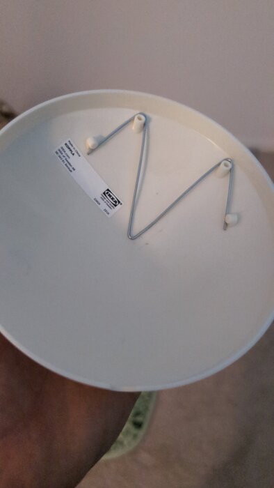 Baksidan av en väggklocka med upphängningskrokar och en etikett från IKEA.