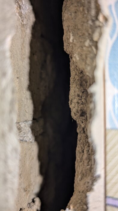 Spricka mellan två väggar i gammalt stenhus, cirka 2-3 cm bred, med tydligt synligt poröst kalkbruk, del av renoveringsprojekt mot möss.