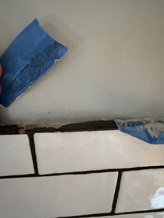 Vit kakelvägg med ett lager blå tejp som delvis täcker den övre kanten, under skåpet i köket.