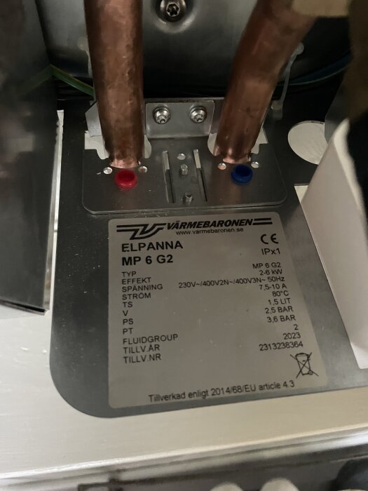 Närbild av en etikett på en Värmebaronen MP6 G2 elpanna med specifikationer och två kopparrör anslutna, en med röd och en med blå markering.