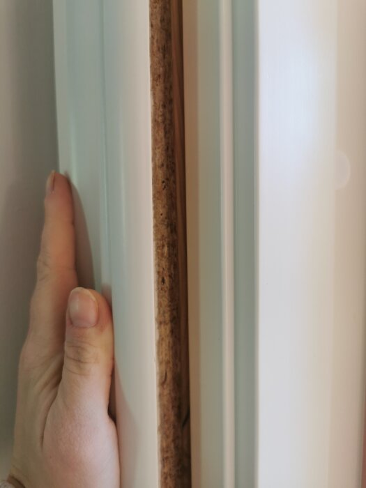 Hand håller i en dörrkarm med synlig glipa mellan fodret och väggen, visar ojämnt hål i utbyggnad.