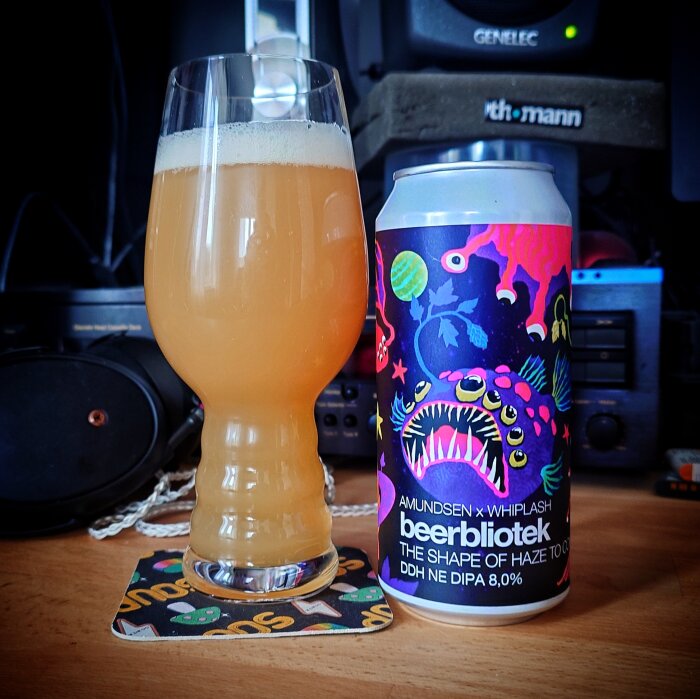 Ett glas med ljus öl bredvid en färgglad ölburk med mönster på ett bord.