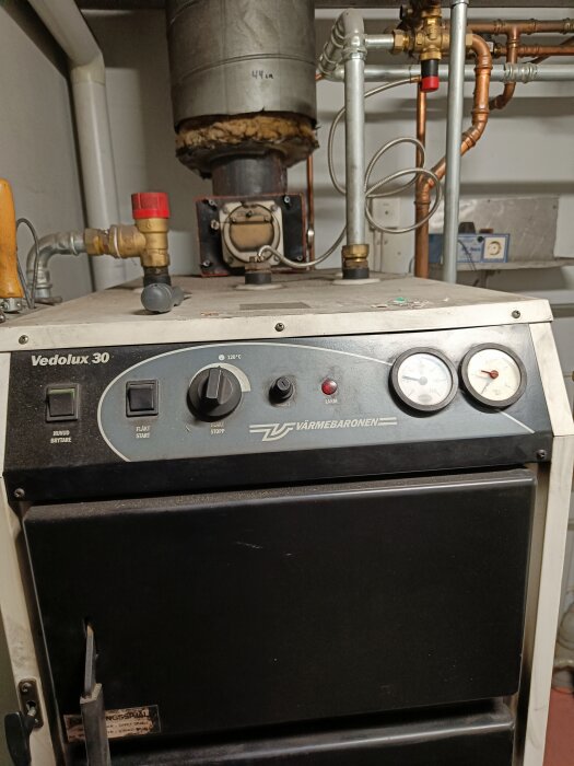 Vedpanna av märket Vedolux 30 med kontrollpanel och rördragning, placerad i ett pannrum.