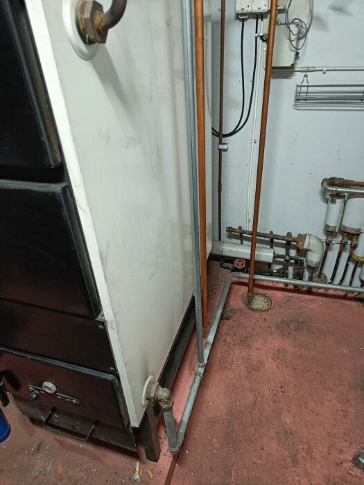 Pannrum med rördragning och pipa ansluten till värmepanna på rosa golv, elkablar på vägg i bakgrunden.