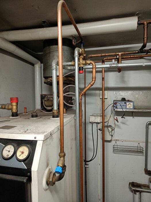 Pannrum med Vedolux 30-panna, kopparrör och mätare, installerad i ett förråd med kopplingar och temperaturregleringsutrustning.