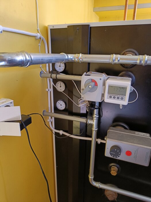 Ackumulatortank med rör och tryckmätare, ansluten till en Thermomatic EC Home enhet, mot en gul vägg i pannrum.