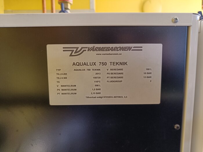 Närbild på en informationsplatta på en Aqualux 750 Tekniktank från Värmebaronen, med specifikationer som tillverkningsår, tryck och volym.