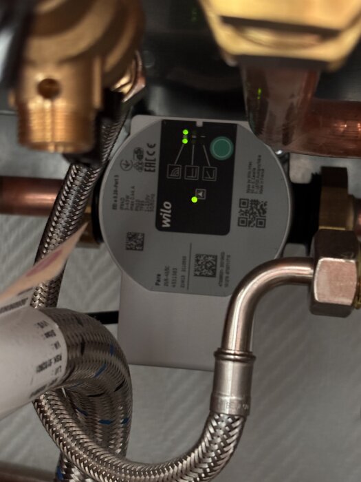 Cirkulationspump under diskbänk med lysande indikatorer och kopparrör, etikett synlig.