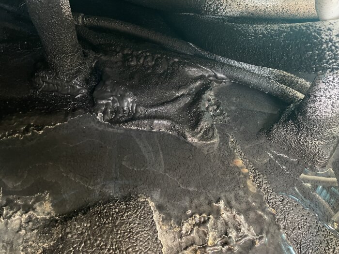 Undersidan av ett spabad där vatten läckt och samlats, med rör och kopplingar synliga. Bakgrunden är mörk och ytan har ojämna strukturer.