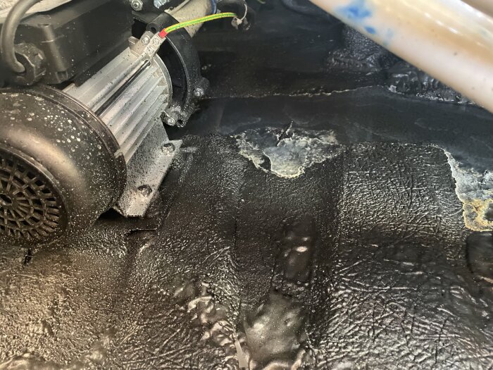 Bild av insidan av ett spabad, visar pump och rör med fuktigt område runtom. Svart yta med fläckar och vätskespår.