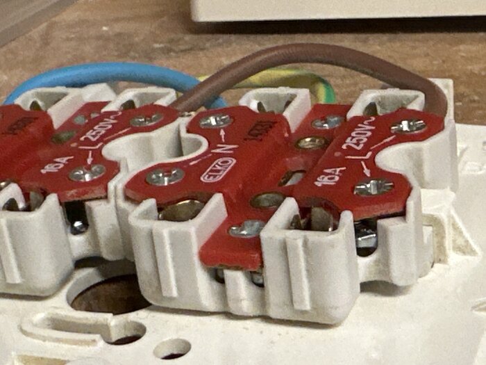 Elko elektrisk kopplingslist med skruvar och kablage på en yta, visar anslutningspunkter för trådar i ett byggprojekt.