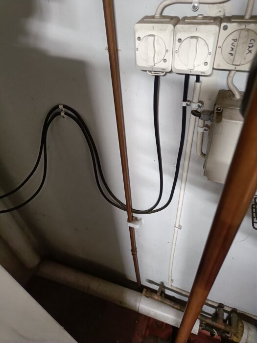 Rörsystem med kopparrör och ett eluttag på en vägg. Finns en rörledningskoppling nära golvet.