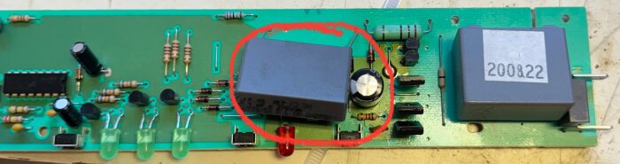 Närbild på ett kretskort med olika komponenter, inklusive en inringad elektrolytkondensator samt X2-kondensator.