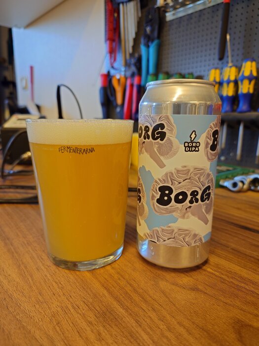 En burk Borg DIPA-öl och ett glas med samma öl på ett bord i en verkstadsmiljö.