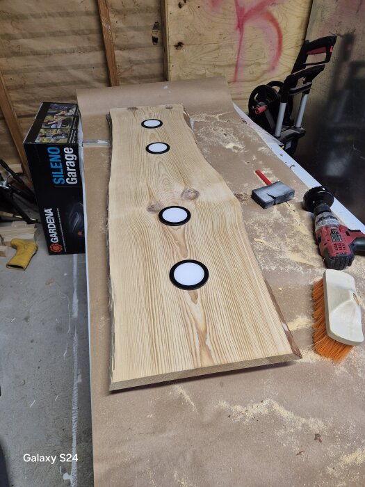 Träbit med fyra infällda lampor på ett arbetsbord, omgivna av verktyg och sågspån, del av ett DIY-taklampaprojekt i utveckling.