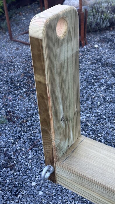 Trädel av båtvagn med borrat hål och metallögla, placerad på grusad mark.