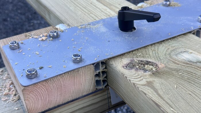 Närbild av en båtvagns konstruktion; träbalk med metallplatta och skruvar, omgiven av träflisor.