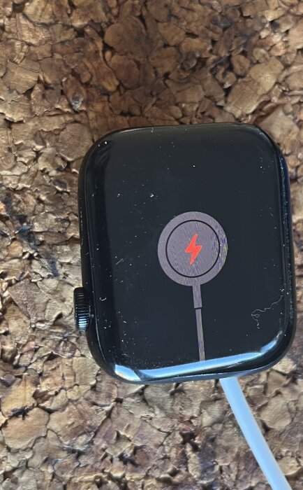 Svart smartklocka som laddas, visad ovanpå ett träliknande underlag.