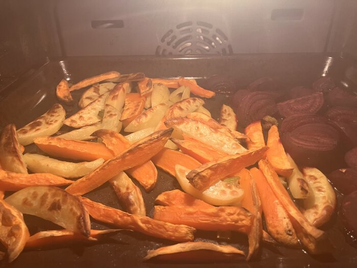 Ugnsrostade potatisklyftor, sötpotatis och rödbetor på en bakplåt.