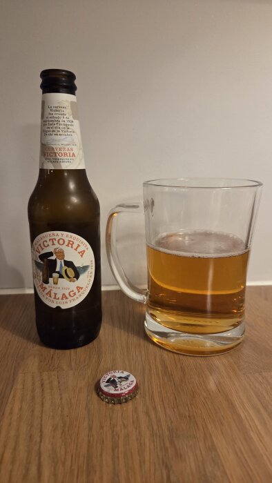 Flaska med Victoria Málaga öl, glas med lager öl och kapsyl på träd yta.