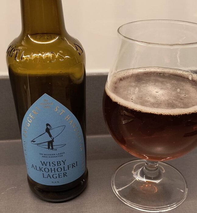 Flaska och glas med Wisby Alkoholfri Lager med gyllenbrunt öl och skumkant.