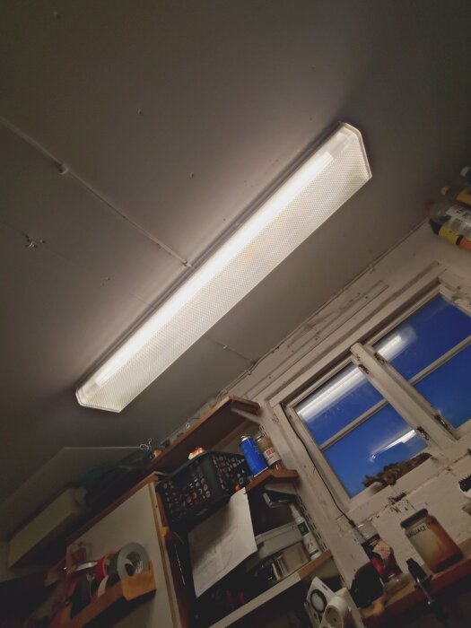 Modernt LED-lysrör installerat i taket i ett rum, med hyllor och ett fönster i bakgrunden.