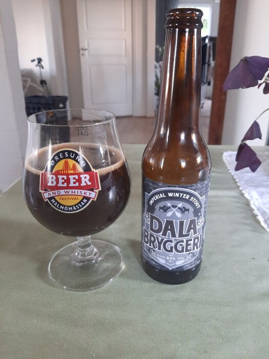 Flaska och glas med Imperial Winter Stout från Dala Bryggeri på ett bord. Glaset är märkt med Öresund Beer and Whisky Festival.