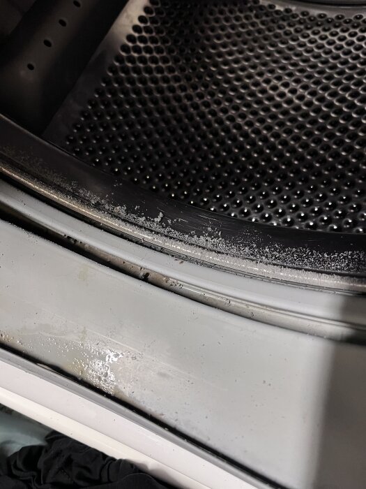 Bild på insidan av en tvättmaskintrumma med små partiklar längs kanten, orsak okänd.