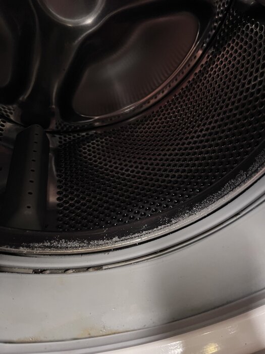 Insidan av en tvättmaskinstrumma med smutsiga rester och beläggningar synliga längs kanterna.