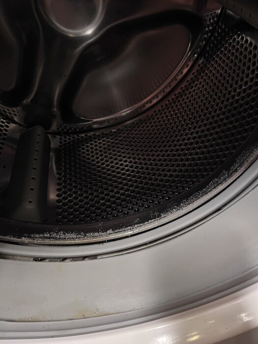 Tvättmaskinens trumma med slitage och klumpar på kanten, eventuellt tecken på skador eller avlagringar.
