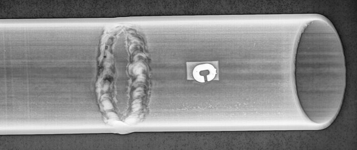 Röntgenbild av ett rör med en skadad del och ett otydligt objekt inuti.