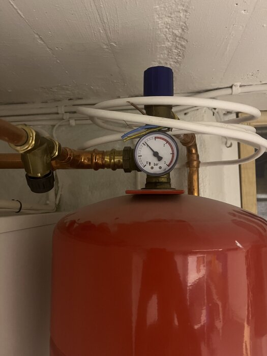 Röd trycktank med manometer visar tryck i bar. Kopparrör och blå komponent ovanpå. Omsluten av vita kablar.