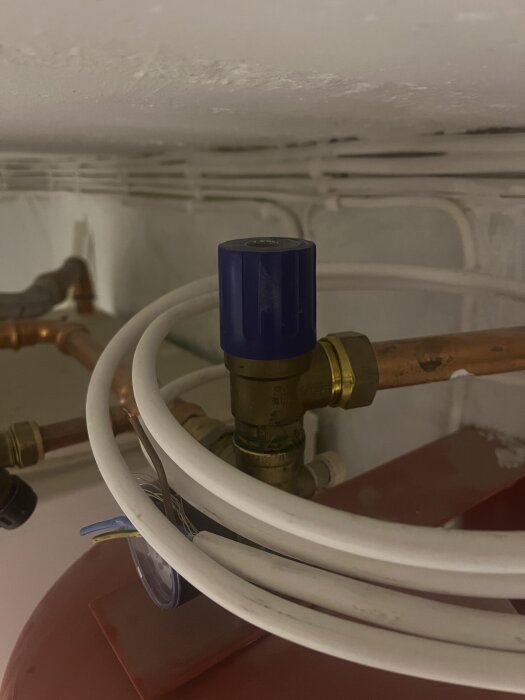 En ventil med en blå komponent monterad på kopparrör omgiven av vita kablar i en byggkonstruktion.