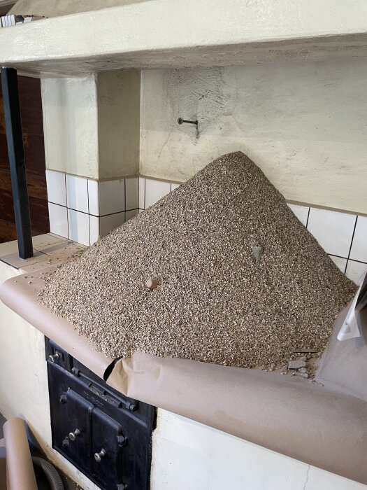 En hög vermiculite har spillts ut över en täckt yta vid en vedspis, med en synlig murad vägg och kakel i bakgrunden.