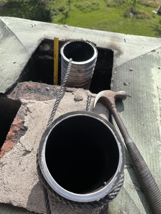 Öppningar i skorsten på hustak med rör, rep och hammare bredvid. Grön mark syns i bakgrunden.