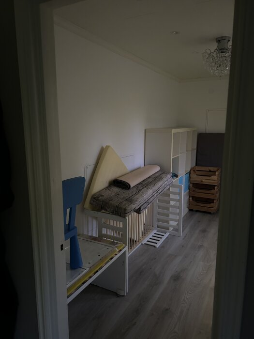 Klädkammare innan renovering, med tomma hyllor och förvaringslådor, en staplad madrass och en liten barnstol.