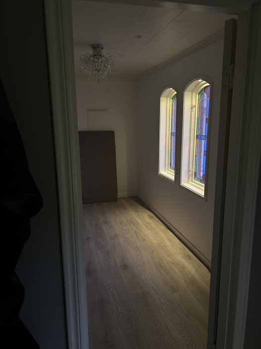 Långt smalt rum med ljusa trägolv, kristallkrona och två fönster. Bild från klädkammare efter renovering.