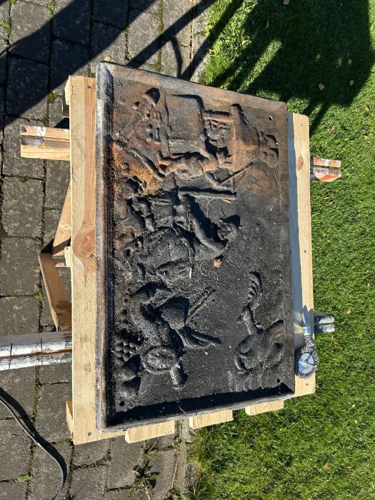 Gammal sättungsplatta med ingraverade bilder, rengjord och liggande på ett bord utomhus, redo för spissvärta; del av renoveringsprojekt.
