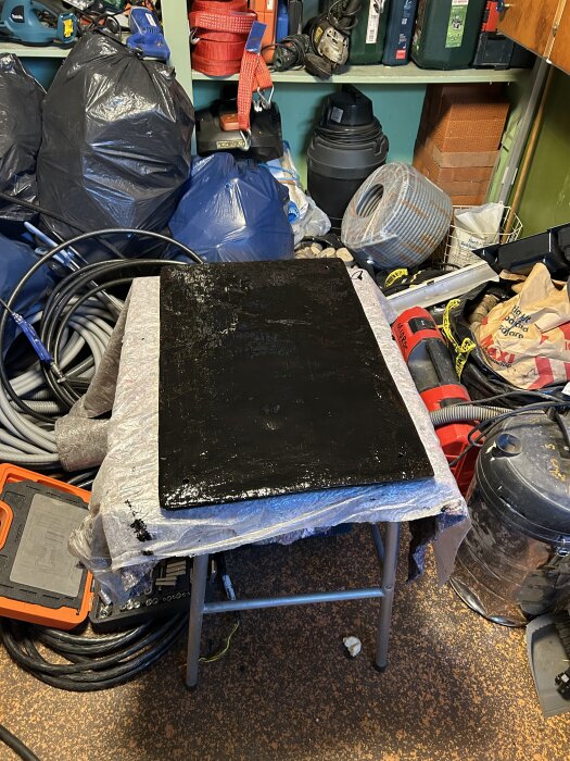 Sättungsplatta målad med hammarlack står på ett bord i en verkstad, omgiven av verktyg och byggmaterial.