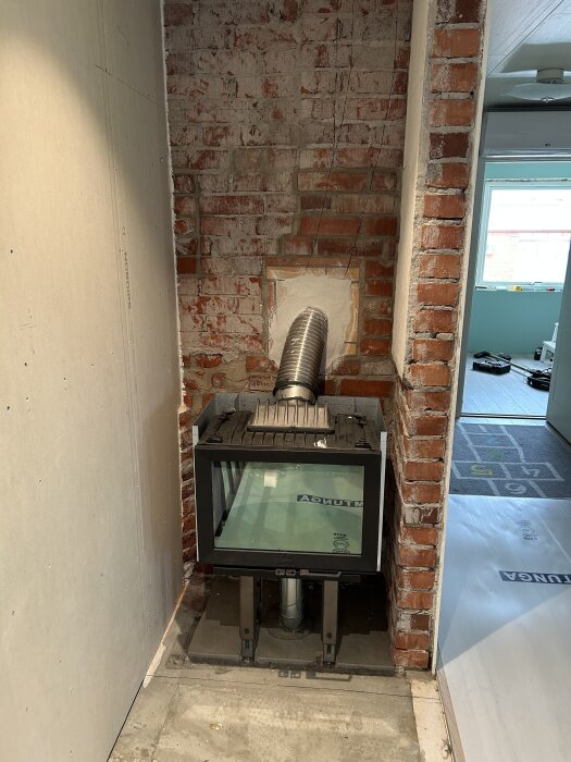 Kamininsats installerad i en halvfärdig tegelvägg med synligt rör för anslutning i en renoveringsmiljö.