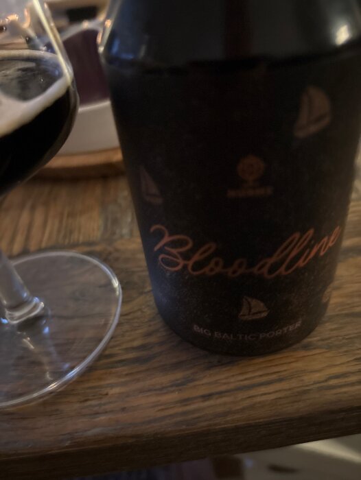 Flaska och glas med mörk öl, märkt "Bloodline Big Baltic Porter", på ett träbord.