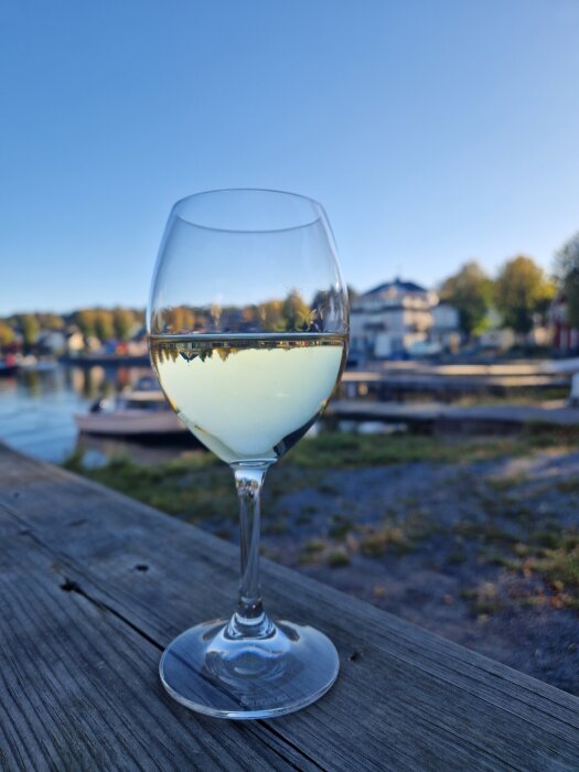Ett glas Riesling på ett träbord utomhus, med en suddig bakgrund av en sjö och byggnader i soligt oktoberväder.