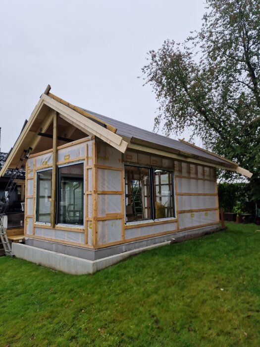 Nybyggt hus med vindduk, skjutdörrar och fönster utan foder. Undertak och vindskivor installerade, huset förberett för kallställning.