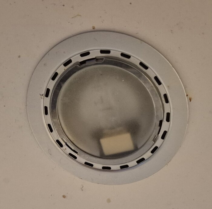 Inbyggd spotlightlampa ovanför en köksbänk, med glas och metallram, delvis ur funktion.