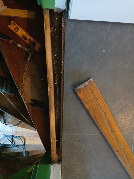 Golvinstallationsprojekt med synlig tröskel och golvöverlappning. Verktyg som hammare och vattenpass ligger bredvid.