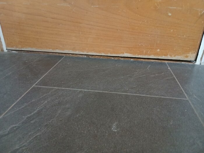 Glipa mellan gammalt tröskel och mörkt golv vid tröskel, där laminatgolv lagts ovanpå undergolv i en hall.