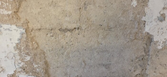 Vägg med flagnande och ojämn puts, varierande i färg och struktur, tecken på tidigare lagningar i en källarrenovering från 1943.